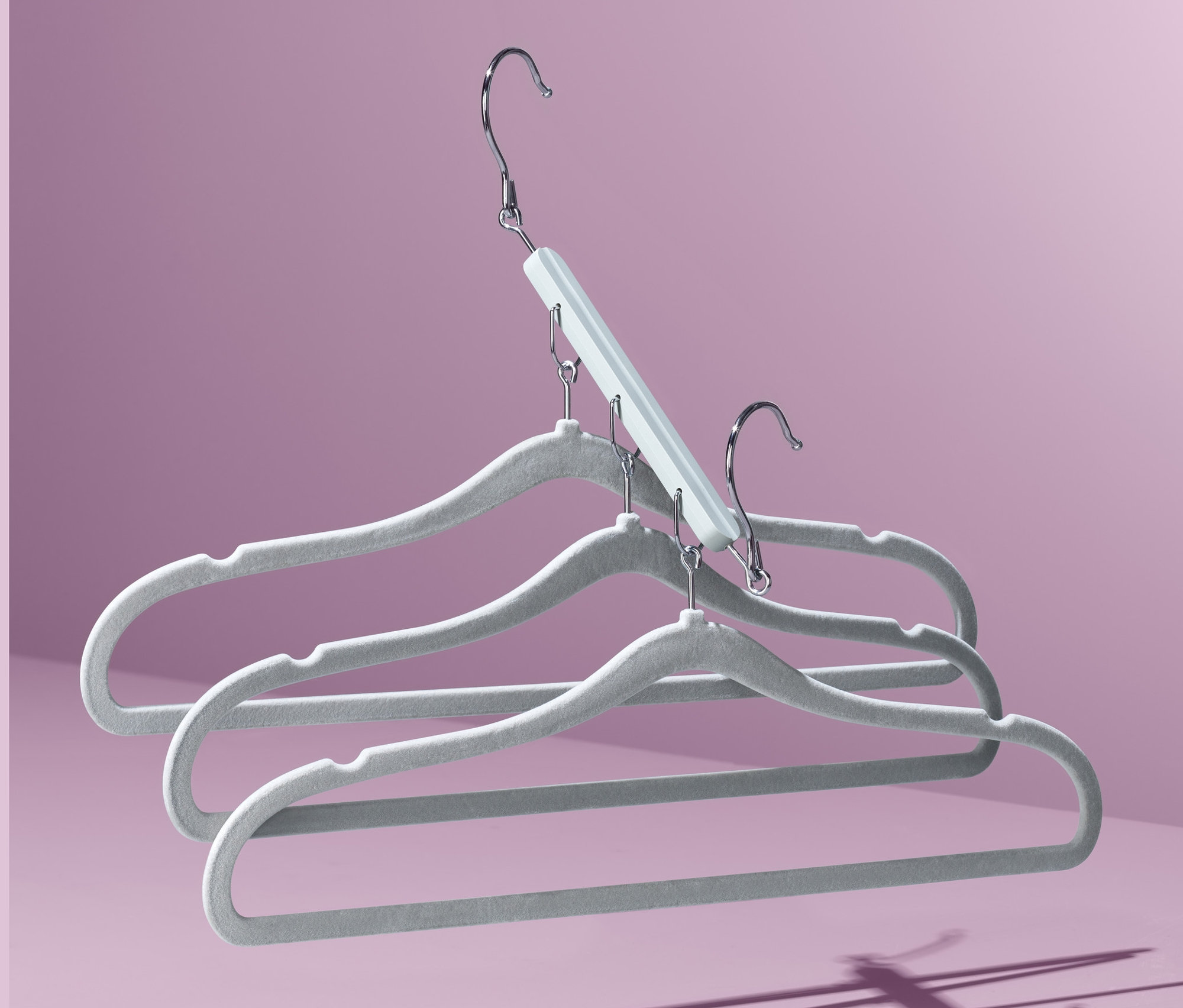 Üç adet alan tasarruflu kıyafet askısı mor bir arka plan üzerinde üst üste duruyor.