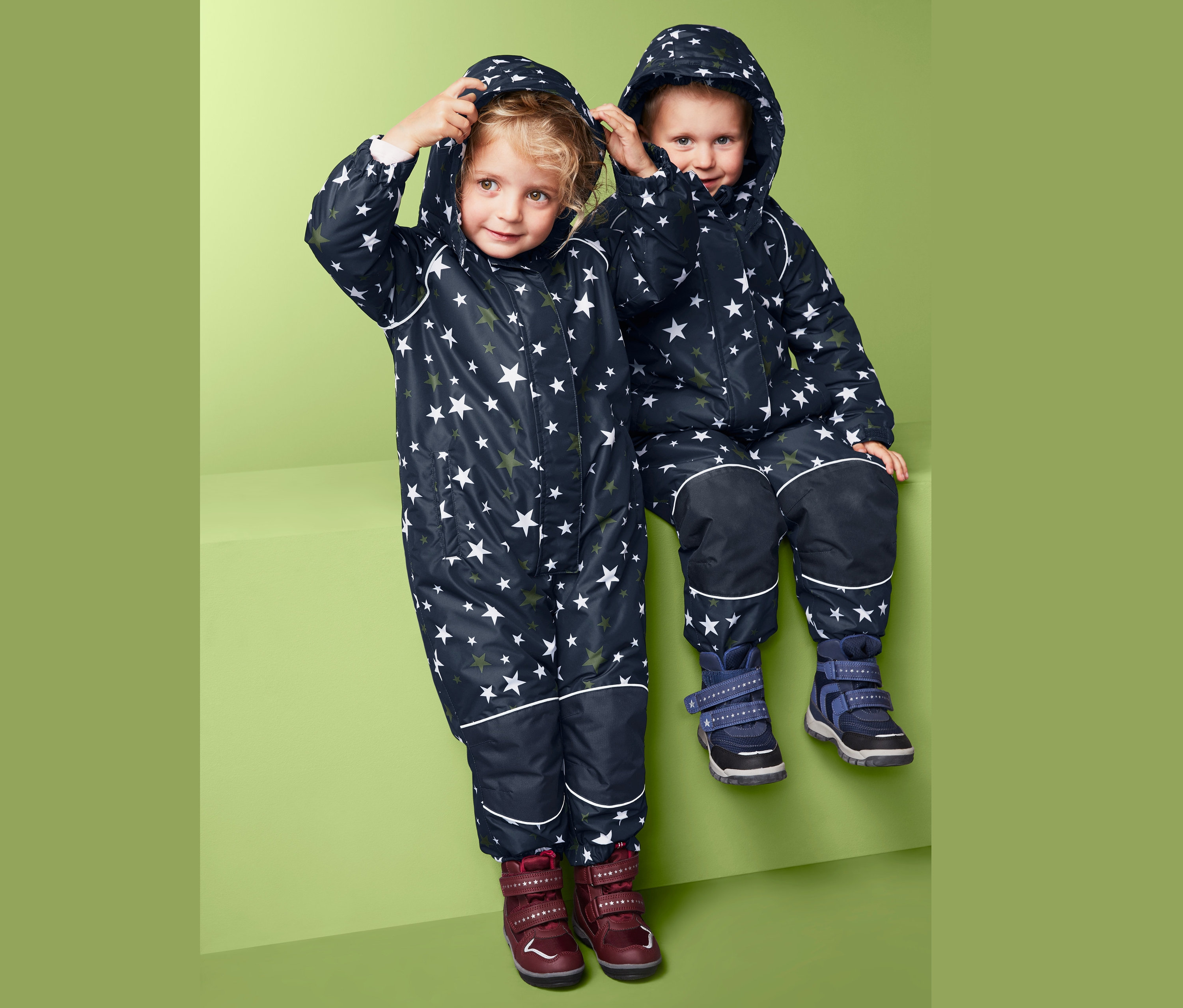 Yıldız desenli kar tulumu giyen çocuklar yan yana oturuyor.