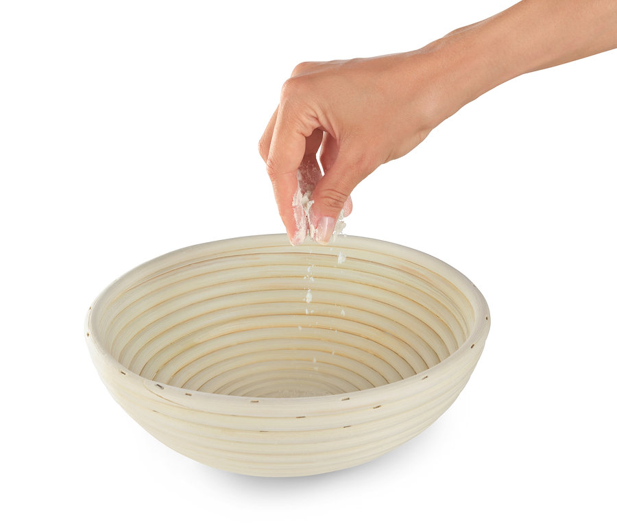 Bir el, yuvarlak mayalama sepetine un serpiyor.