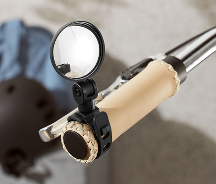 Gidon üzerine monte edilmiş mini bisiklet aynası olan bir bisikletin yakın çekimi. Arka planda bir kask ve ceket görülebilir.