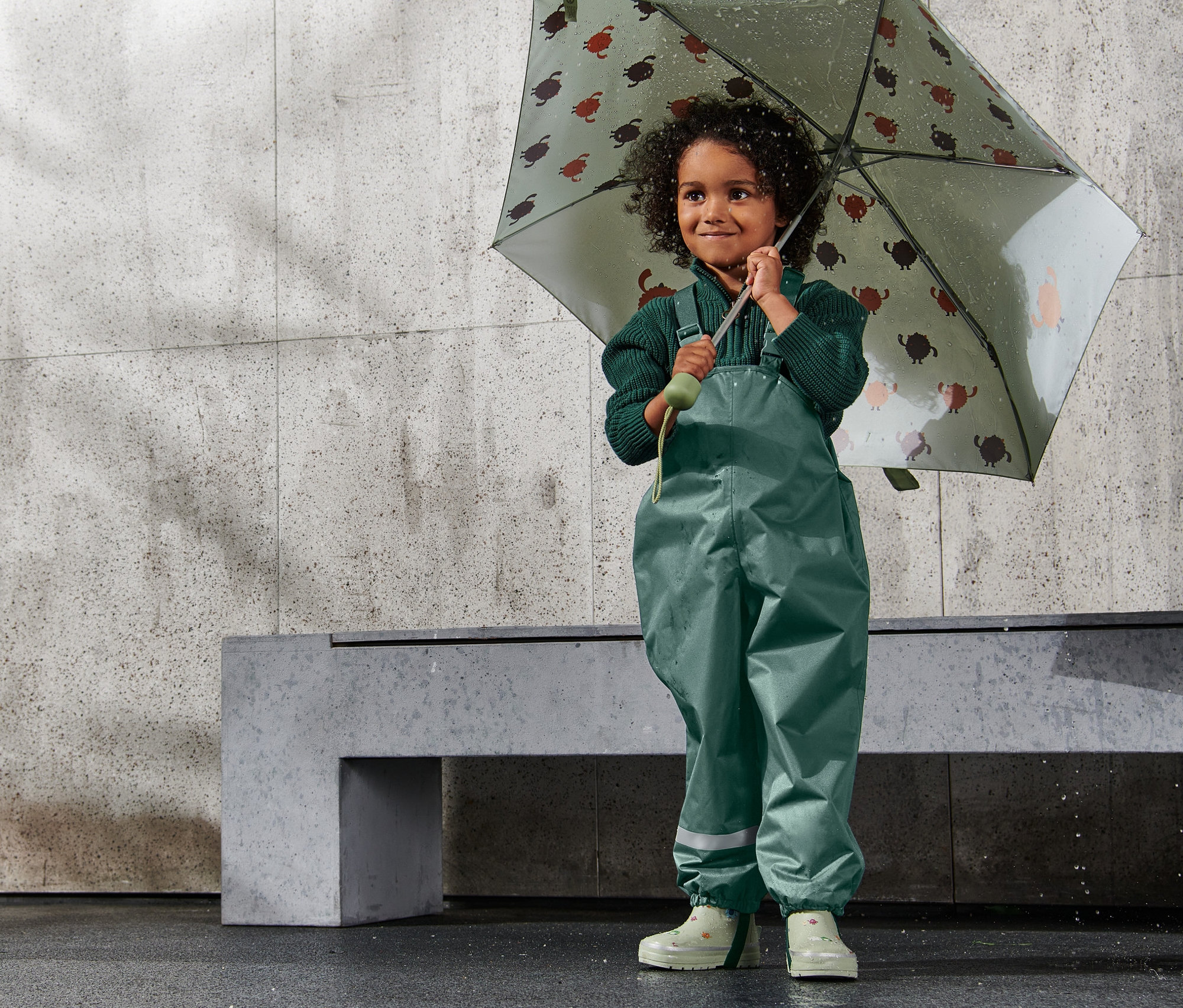 Kız çocuğu kaplumbağa desenli bir şemsiye tutuyor. Üzerinde Çocuk Termal Yağmur Pantolonu, Koyu Yeşil var.