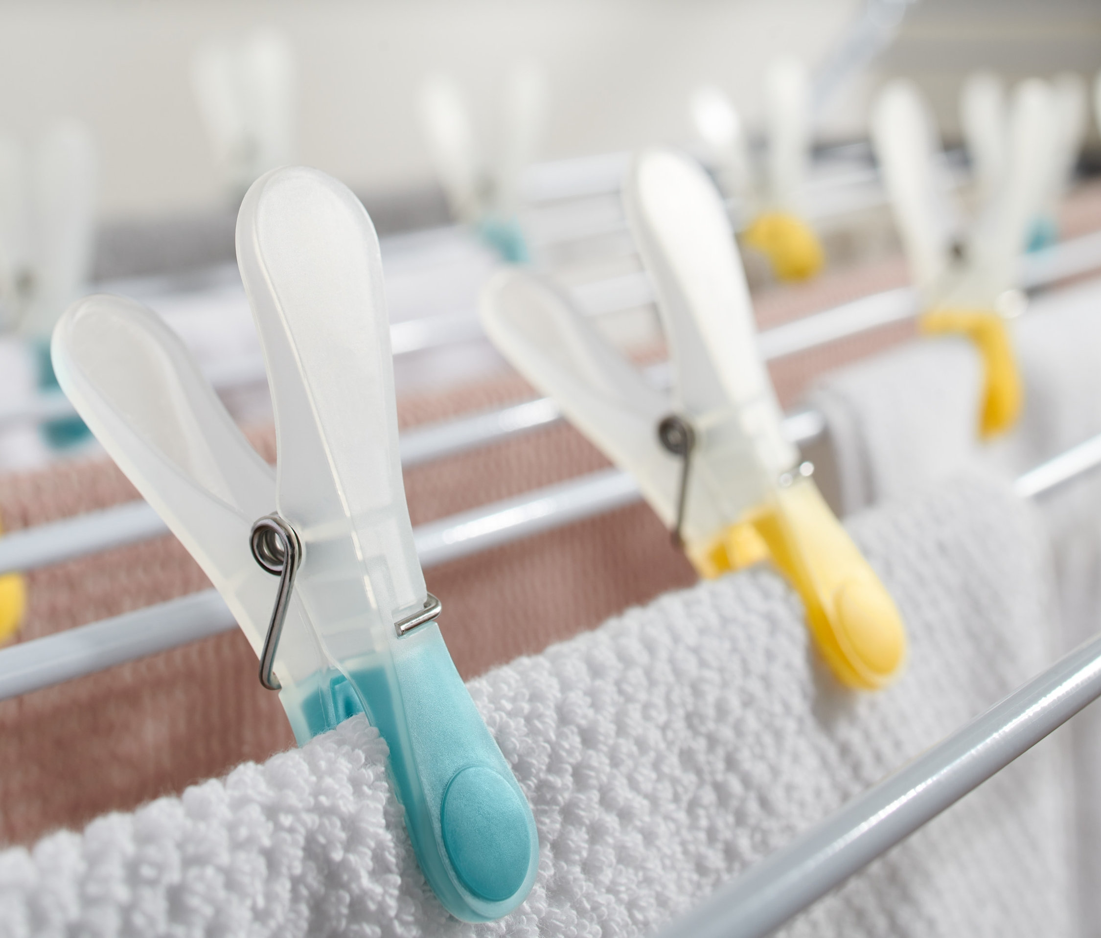 Beyaz ve pembe çamaşırları tutan renkli 20 Adet Çamaşır Mandalı ile beyaz bir çamaşır kurutmalığının yakın çekimi.