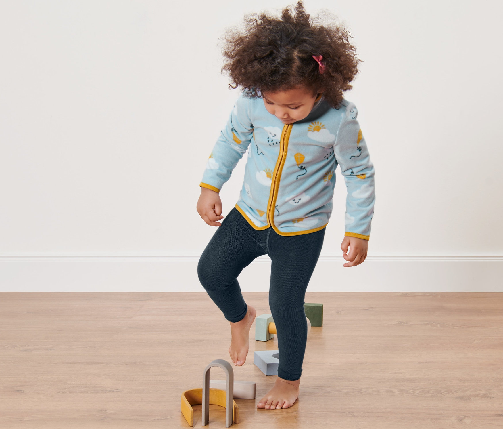 Kız çocuk yerde ahşap oyuncakların üzerine basıyor. Üzerinde 2 Adet Çocuk Örgü Tayt var.