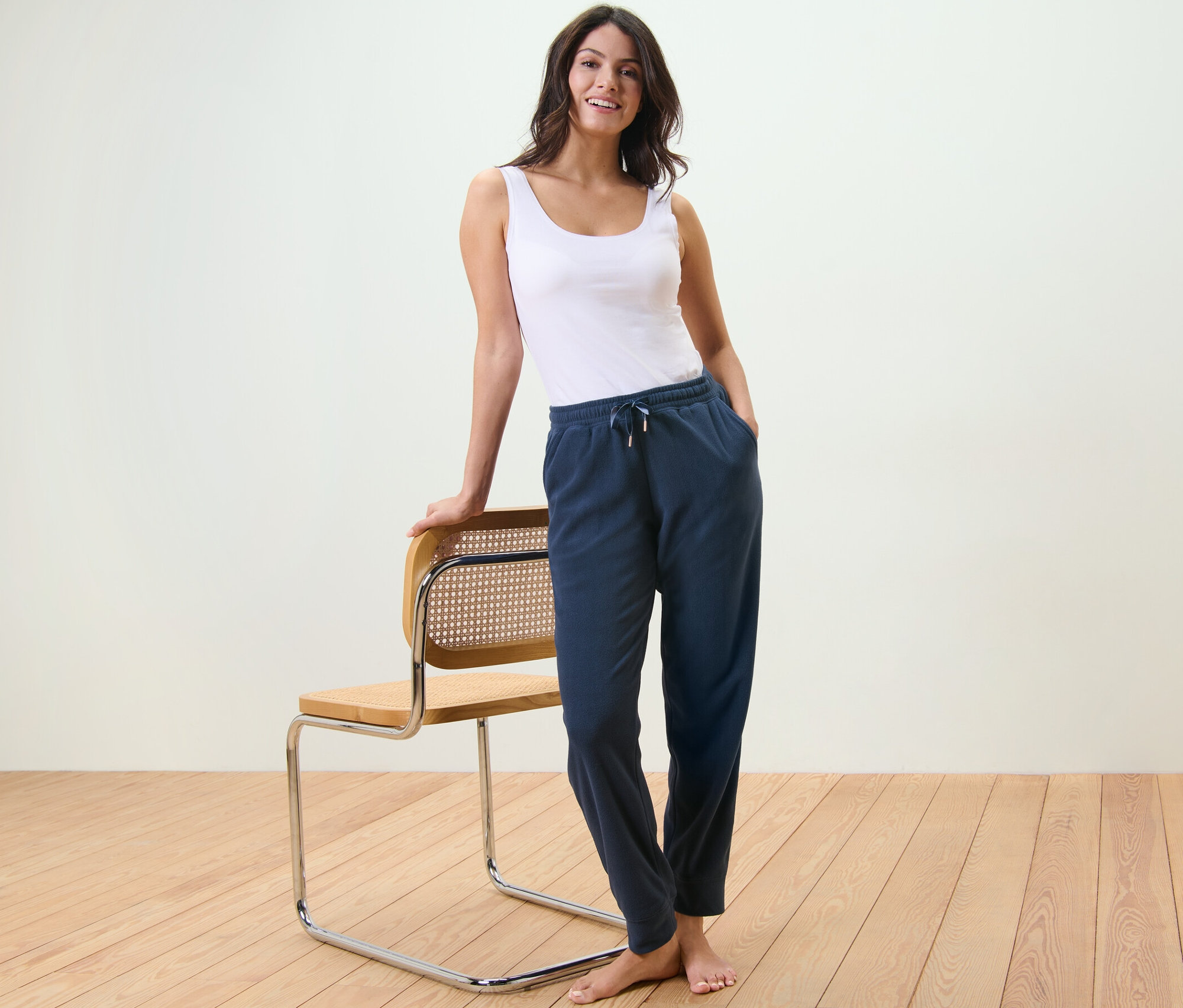 Kadın bir sandalyeye yaslanmış, atlet ve polar eşofman altı giyiyor.