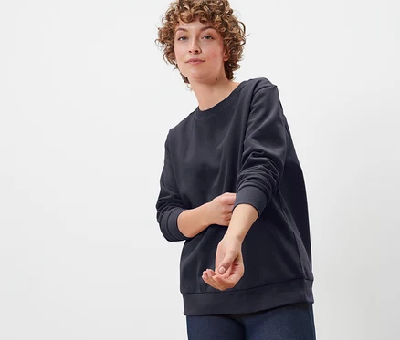 Kıvırcık saçlı bir kadın lacivert organik pamuklu sweatshirt giyiyor.