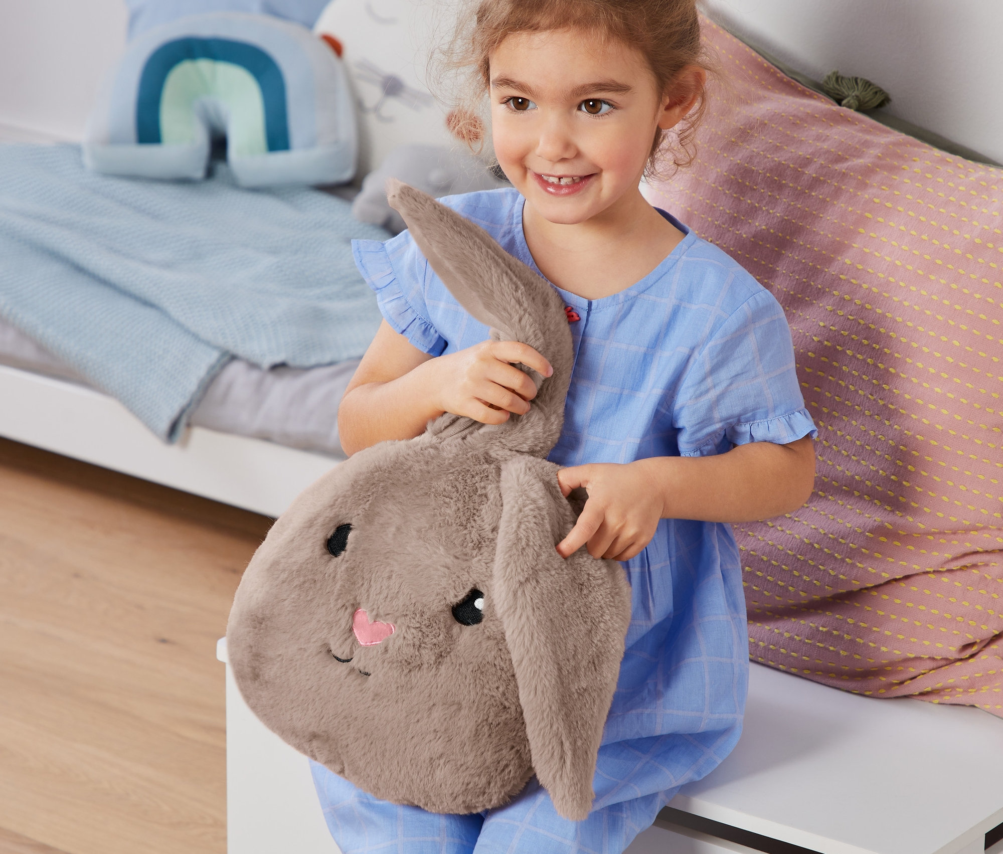 Mavi pijamalı gülen kız çocuğu Pelüş Tavşan Yastık tutuyor.