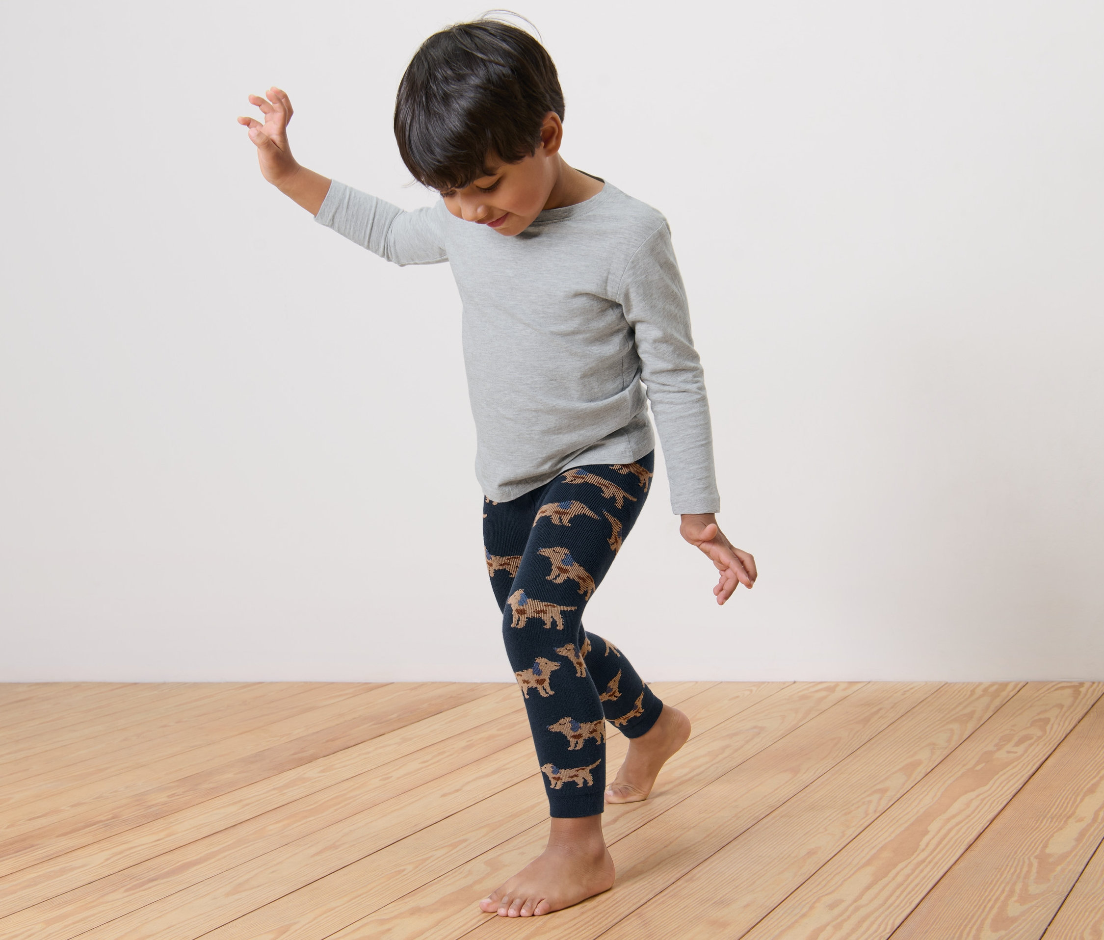 Bir çocuk, üzerinde dachshund deseni olan termal taytla dans ediyor.