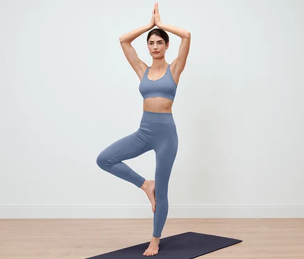 Mavi Dikişsiz Taytlı kadın yoga matı üzerinde ağaç duruşunda duruyor.
