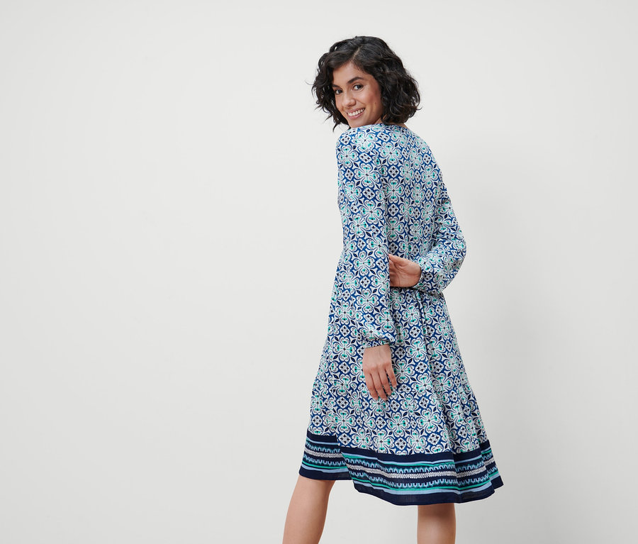 Kadın omzunun üzerinden bakıyor ve tamamı baskılı dokuma bir elbise giyiyor.