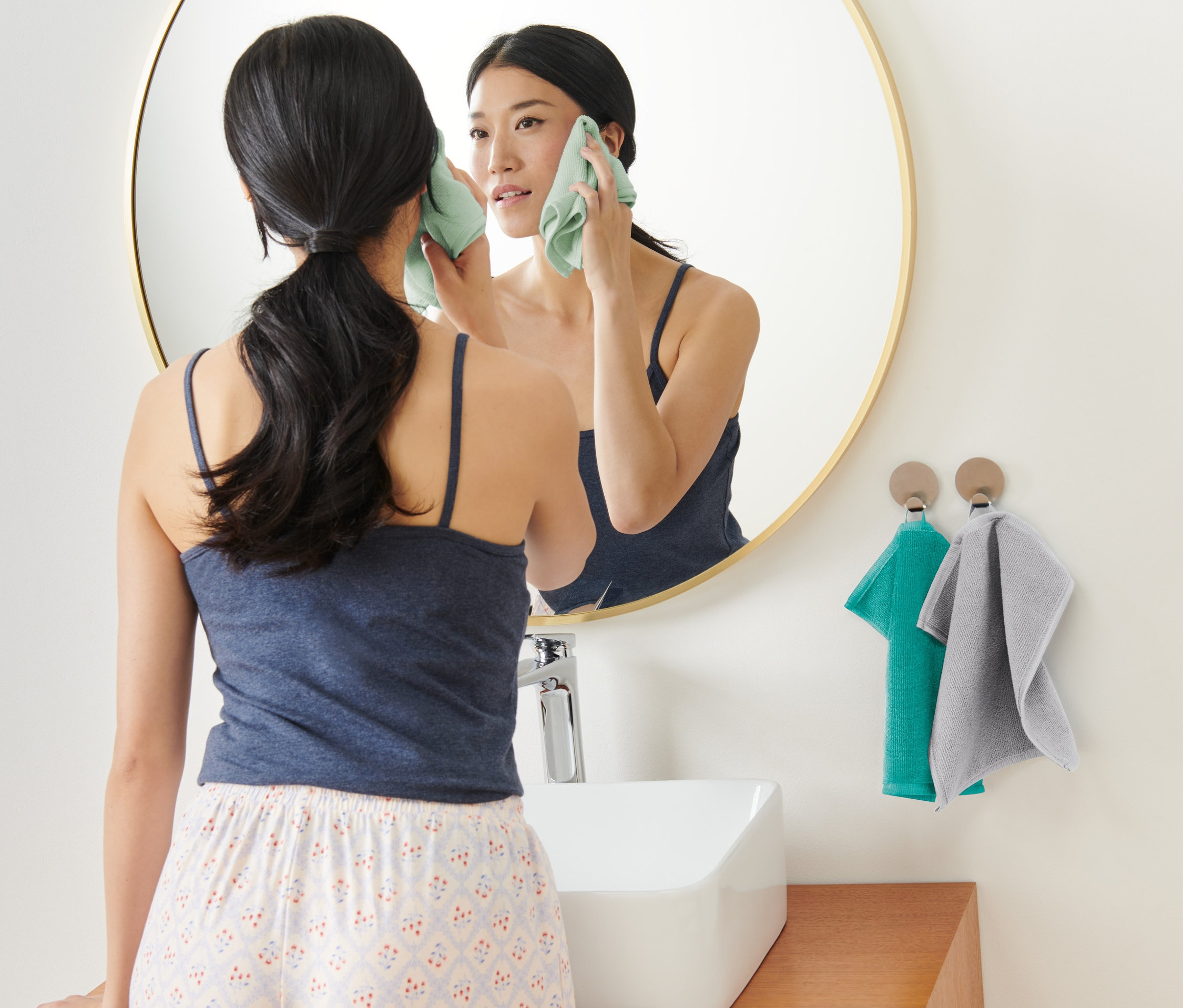 Kadın aynanın önünde 3'lü Mikrofiber Makyaj Temizleme Havlusu ile yüzünü temizliyor.