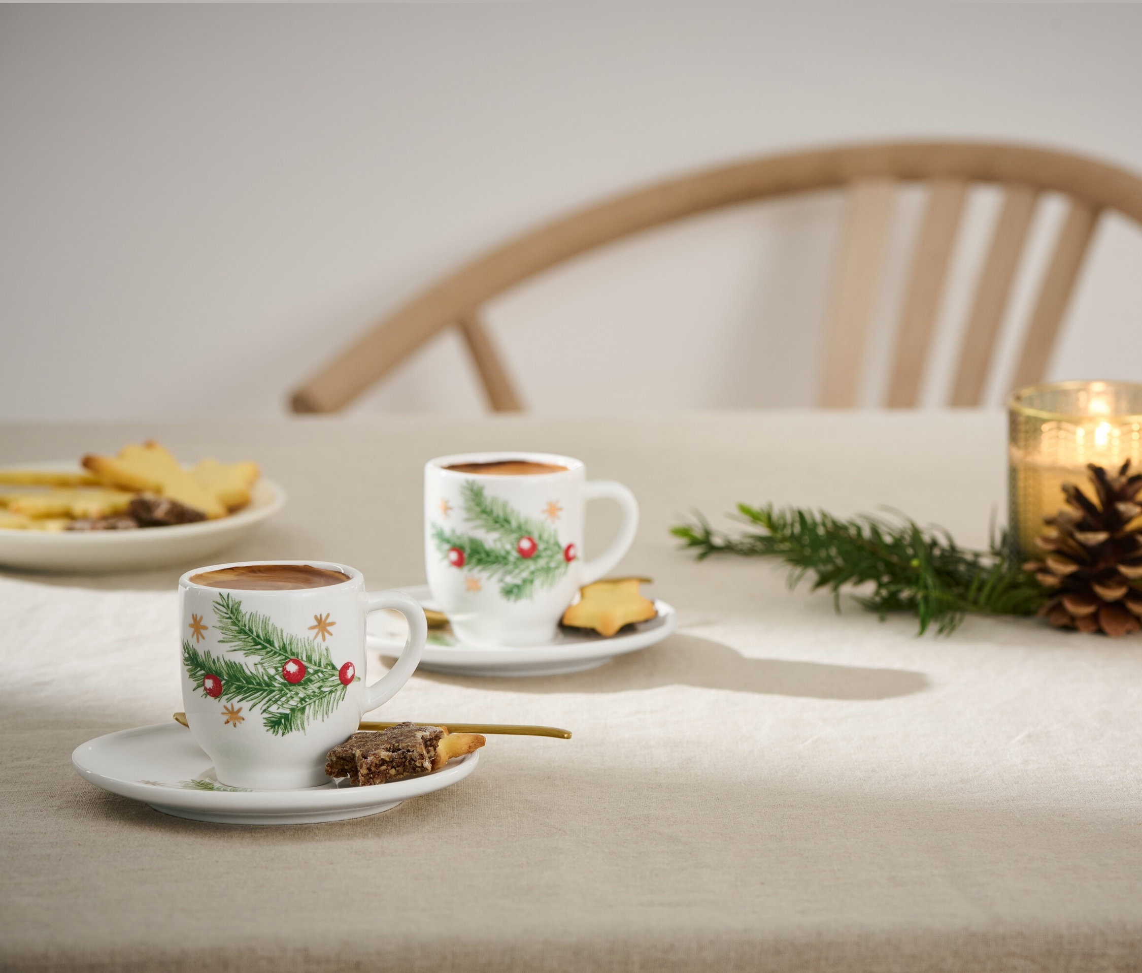 Kurabiye ve mumlarla birlikte masanın üzerinde Noel temalı iki adet espresso fincanı.