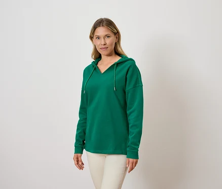 Kadın yeşil kapüşonlu sweatshirt ve açık renk pantolon giyiyor.