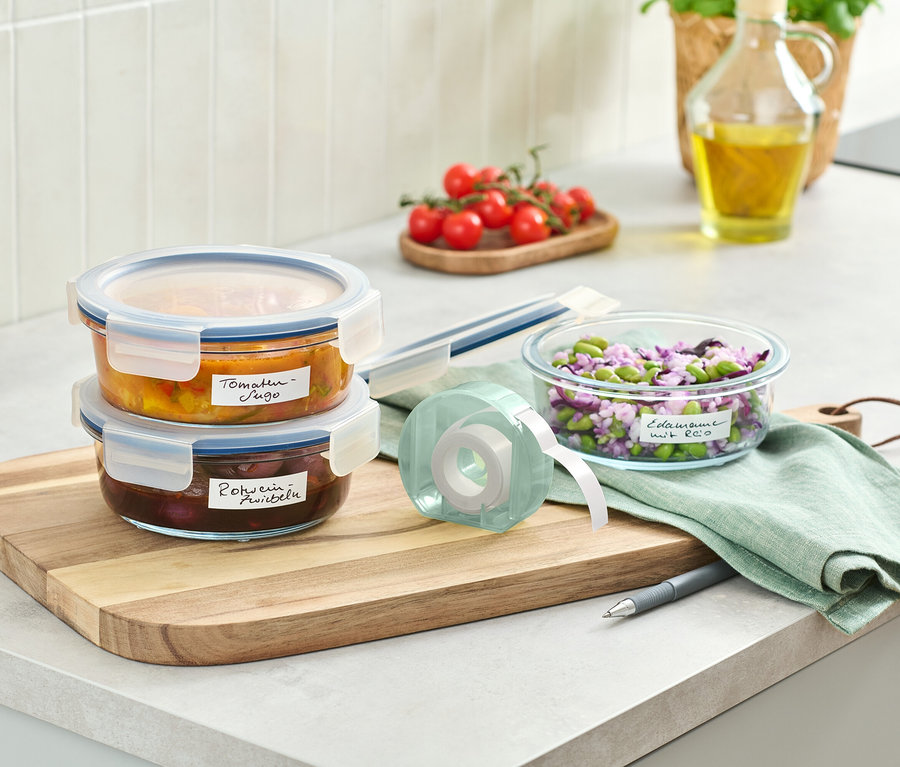 Ahşap bir kesme tahtası üzerinde üst üste istiflenmiş iki cam kap ve bir etiket rulosu.