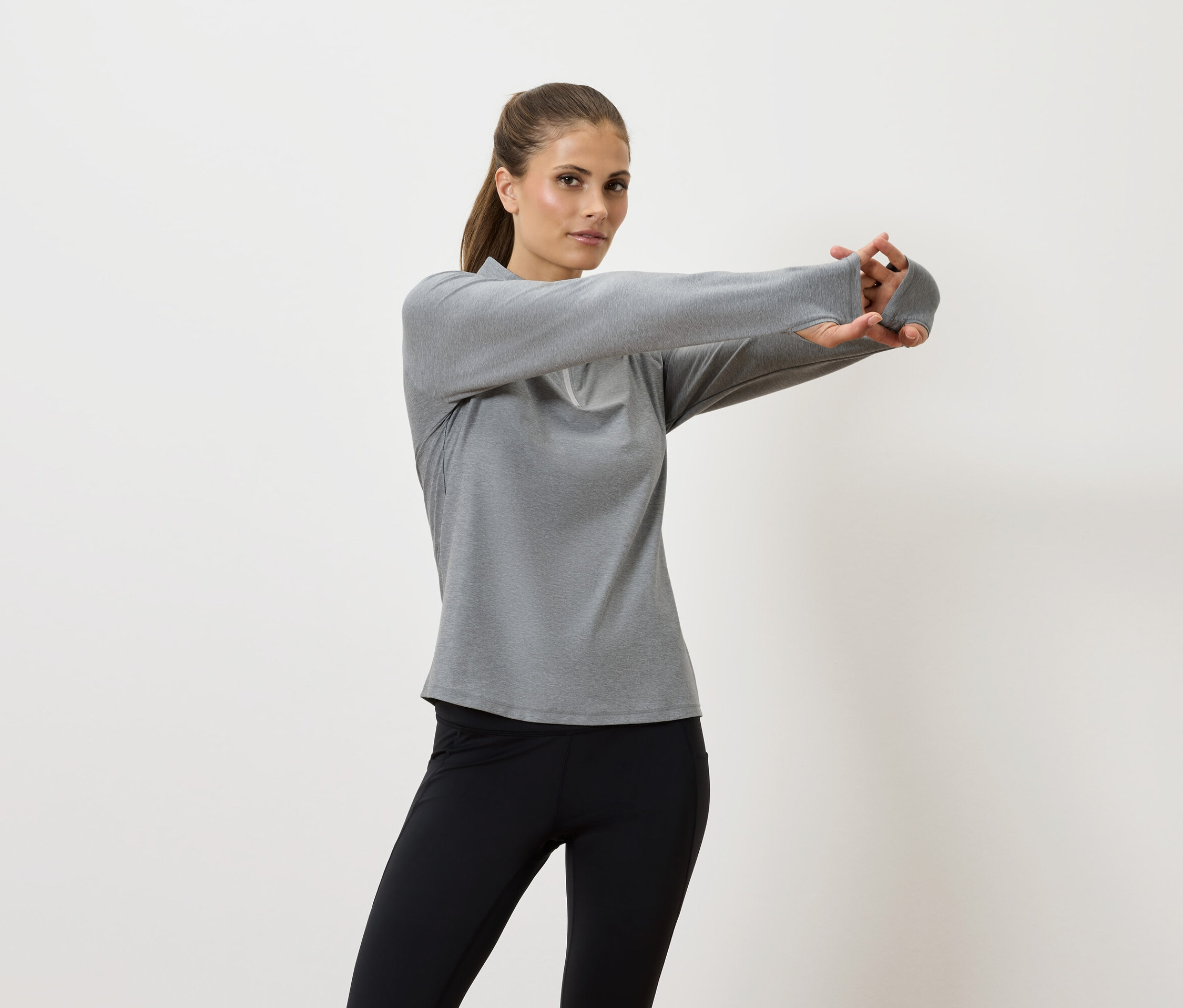 Kadın gri uzun kollu tişört ve siyah taytla kollarını geriyor.