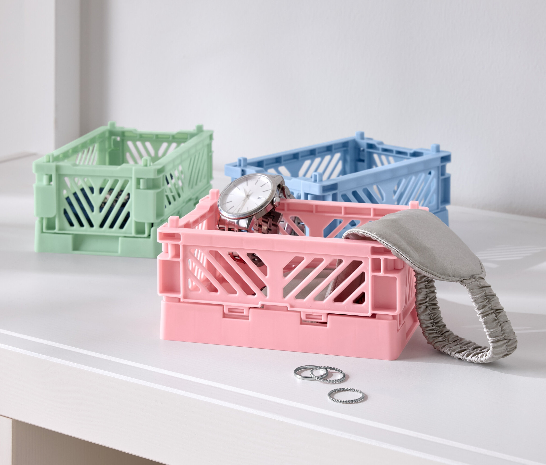 Masanın üzerinde üç renkli katlanır kutu, biri pembe saatli, biri mavi ve biri yeşil.