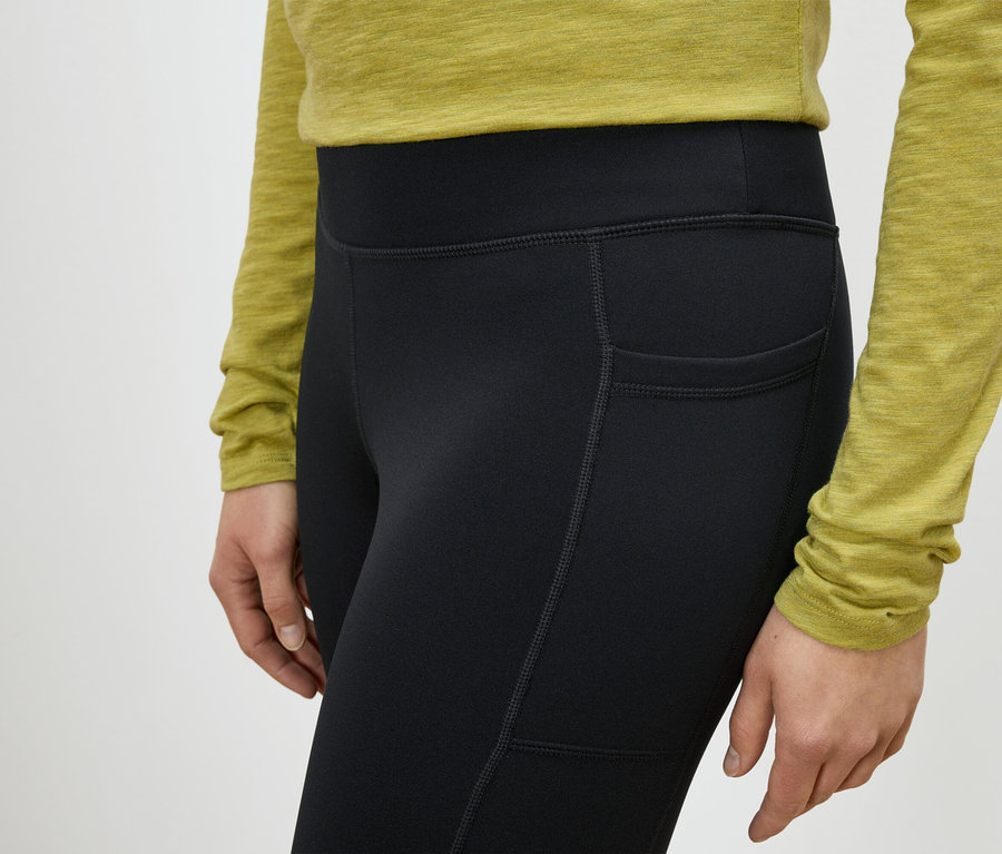 Kadın uyluk cebi olan siyah tayt giyiyor.