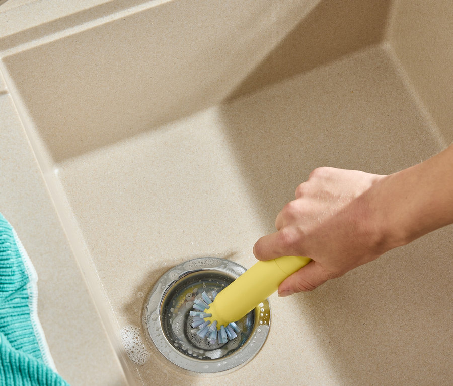 Bir el lavabo giderini sarı bir fırçayla temizliyor. Solda turkuaz bir bez var.