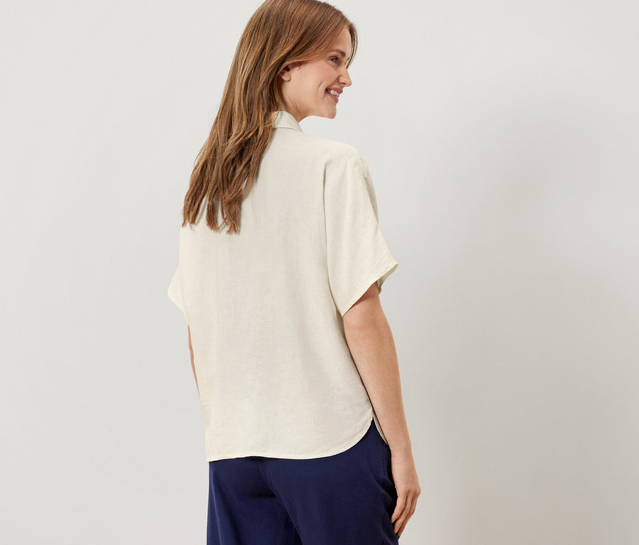 Arkası dönük duran bir kadın krem rengi keten bir bluz giyiyor.