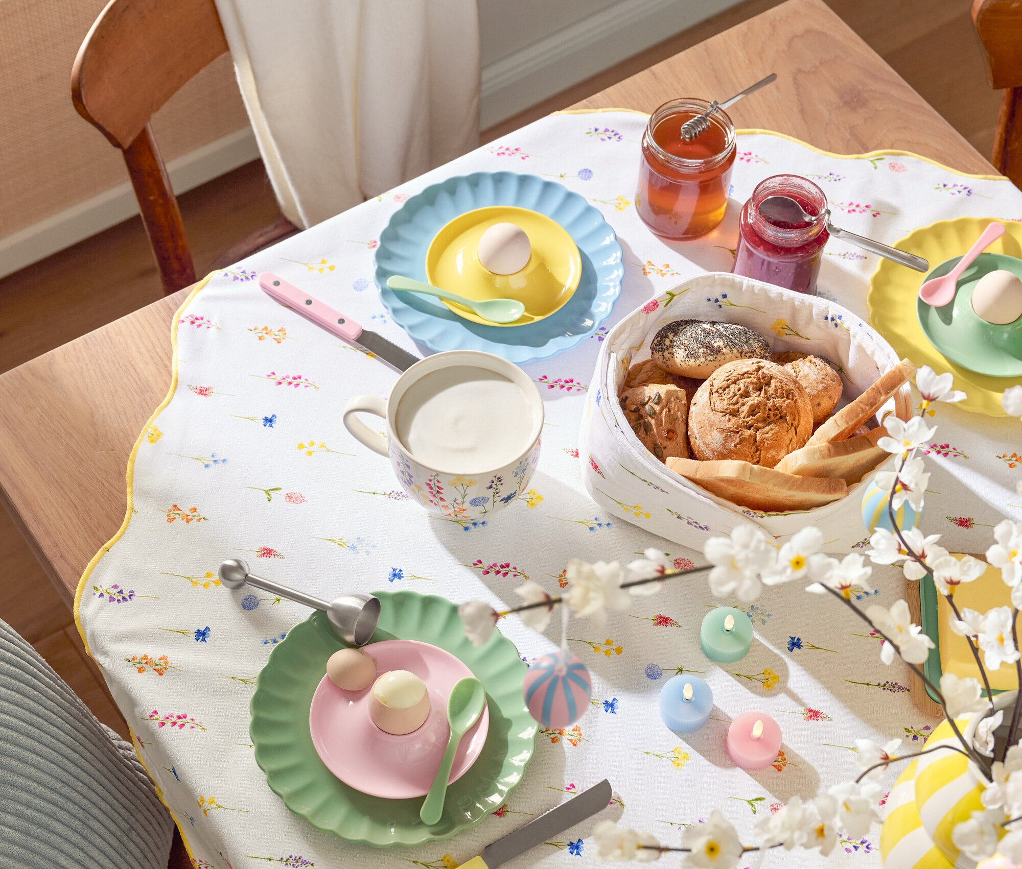 Yemek masası; tabaklar, yumurtalar, kupalar, çatal bıçak takımı, ekmek sepeti, reçel kavanozları, Paskalya süslemeleri ve çiçekli bir masa örtüsü dahil olmak üzere sofra takımı ile birlikte.