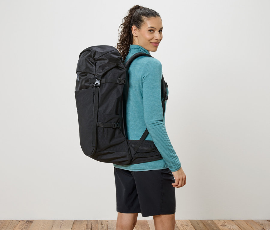 Omuzlarında asılı siyah bir sırt çantası olan ve omzunun üzerinden bakan kadın.