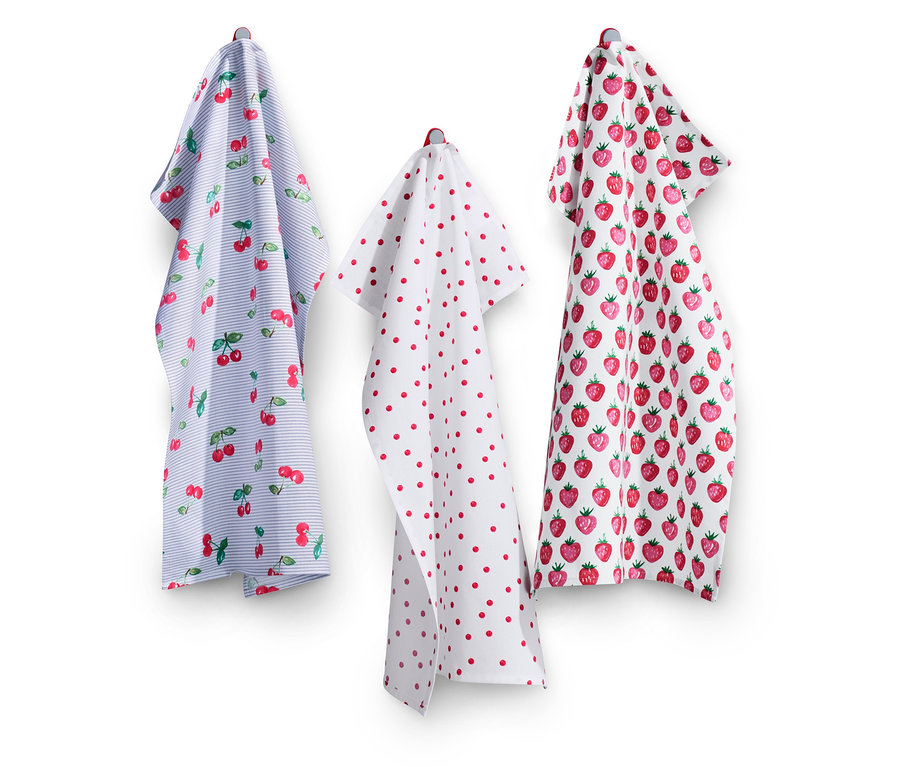 Duvarda asılı üç adet bulaşık bezi. Biri kirazlı mavi, biri kırmızı noktalı beyaz ve biri çilekli beyaz.