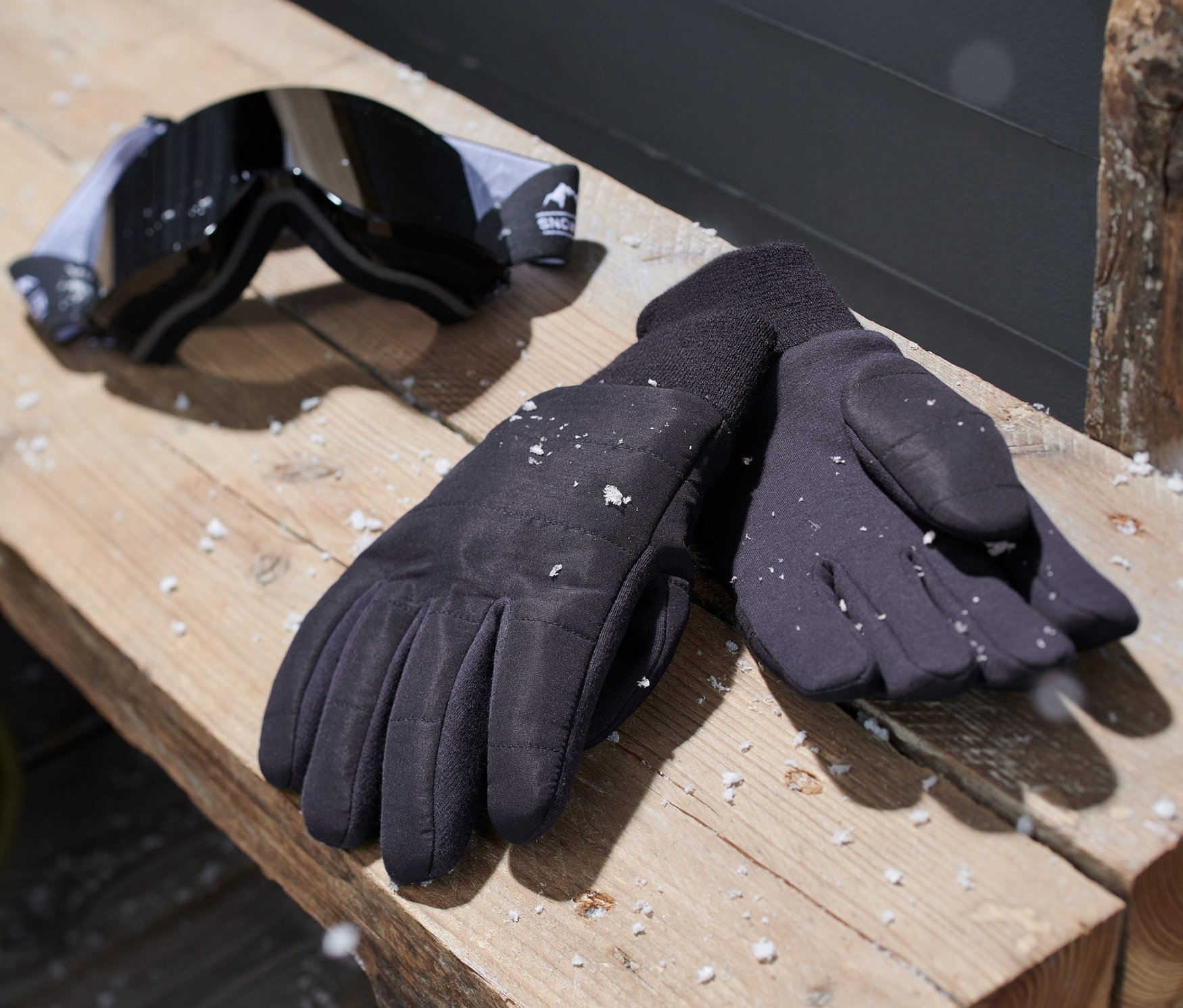 Siyah örgü eldiven ve bir kayak gözlüğü ahşap bir bankın üzerinde duruyor.