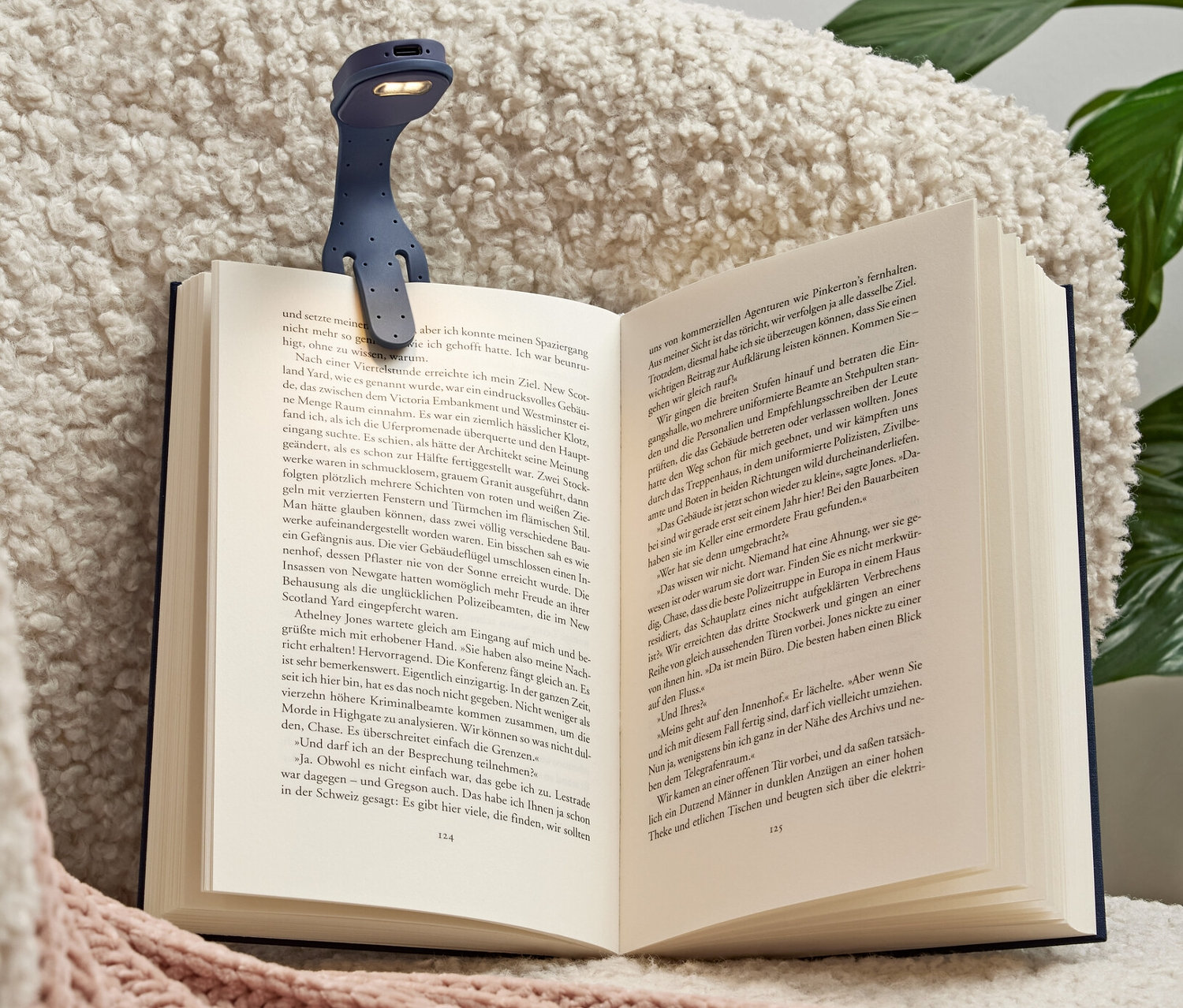 Mavi şarjlı LED mini okuma lambası, koltukta duran açık bir kitaba takılı.