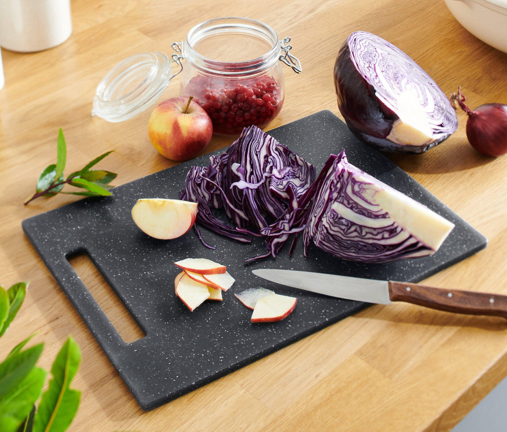 Doğranmış kırmızı lahana ve elmalar, bıçakla birlikte granit görünümlü bir kesme tahtası üzerinde duruyor.