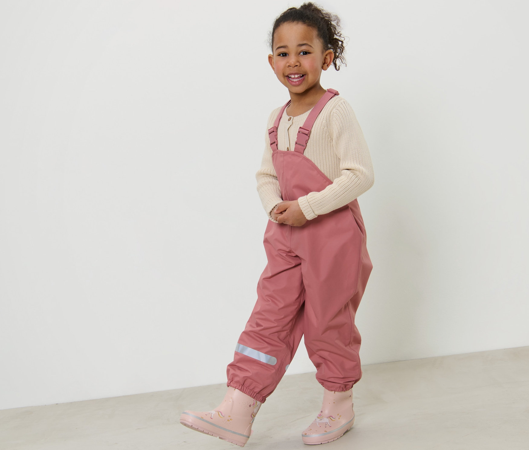 Gülümseyen küçük kız, koyu pembe Çocuk Termal Yağmur Pantolonu ile poz veriyor.