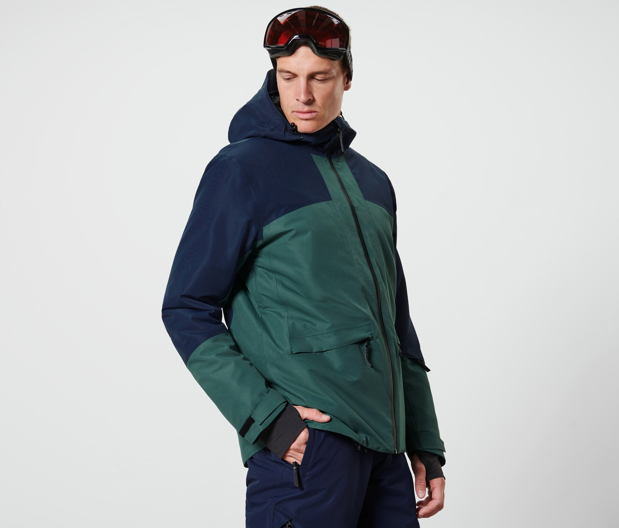 Adam mavi/yeşil bir kayak montu giyiyor.