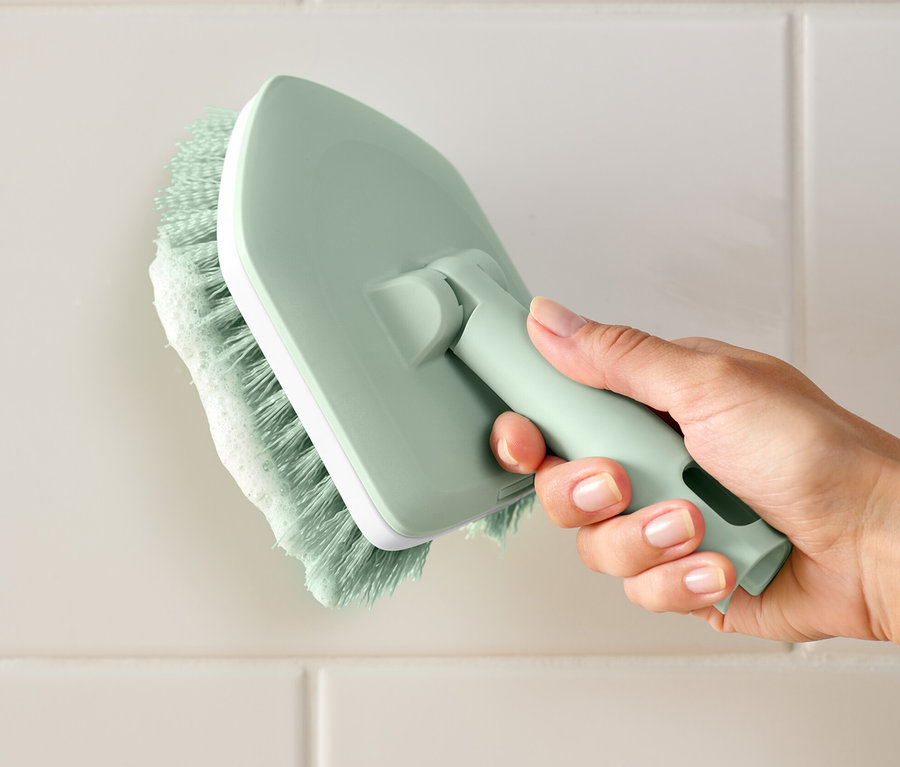 Bir el Fayans ve Banyo Fırçası tutuyor ve beyaz fayansları temizliyor.