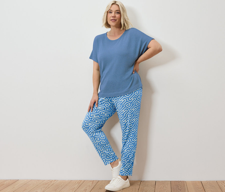 Sarışın bir kadın, mavi baskılı jarse pantolon ve mavi, dokulu bir tişörtle poz veriyor.