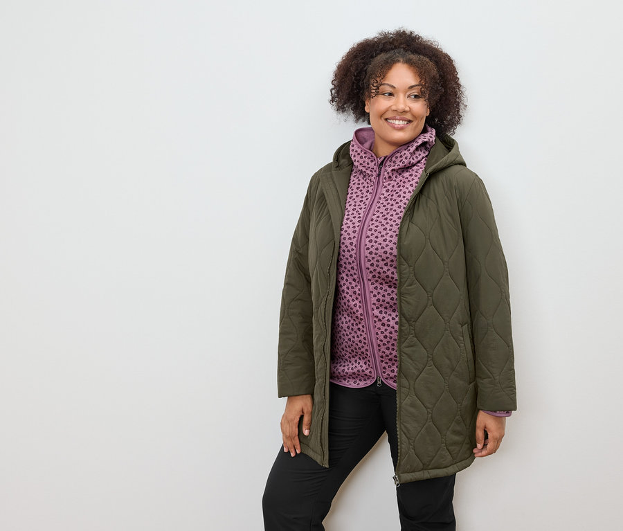 Zeytin yeşili kapitone mont ve mor desenli kapüşonlu sweatshirt giyen kadın.