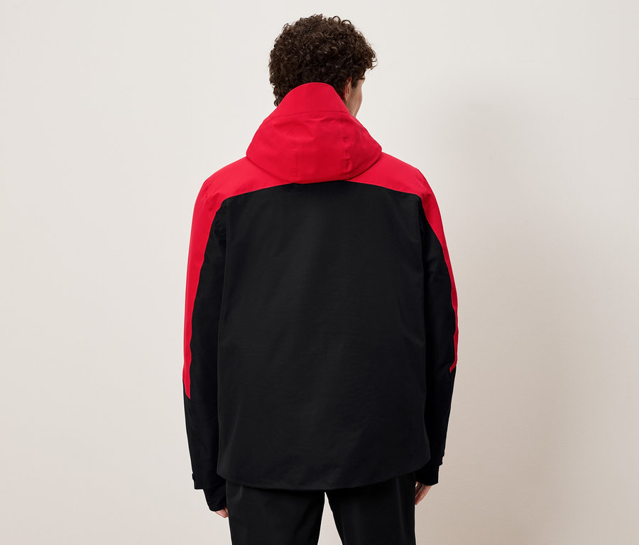 Arkası dönük bir adam siyah ve kırmızı kapüşonlu bir ceket giyiyor.