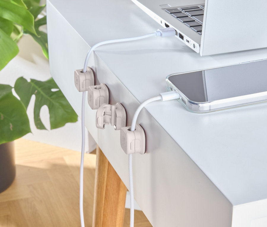 Gümüş rengi dizüstü bilgisayar ve telefon, ahşap kablo tutucularıyla beyaz bir masada şarj oluyor.