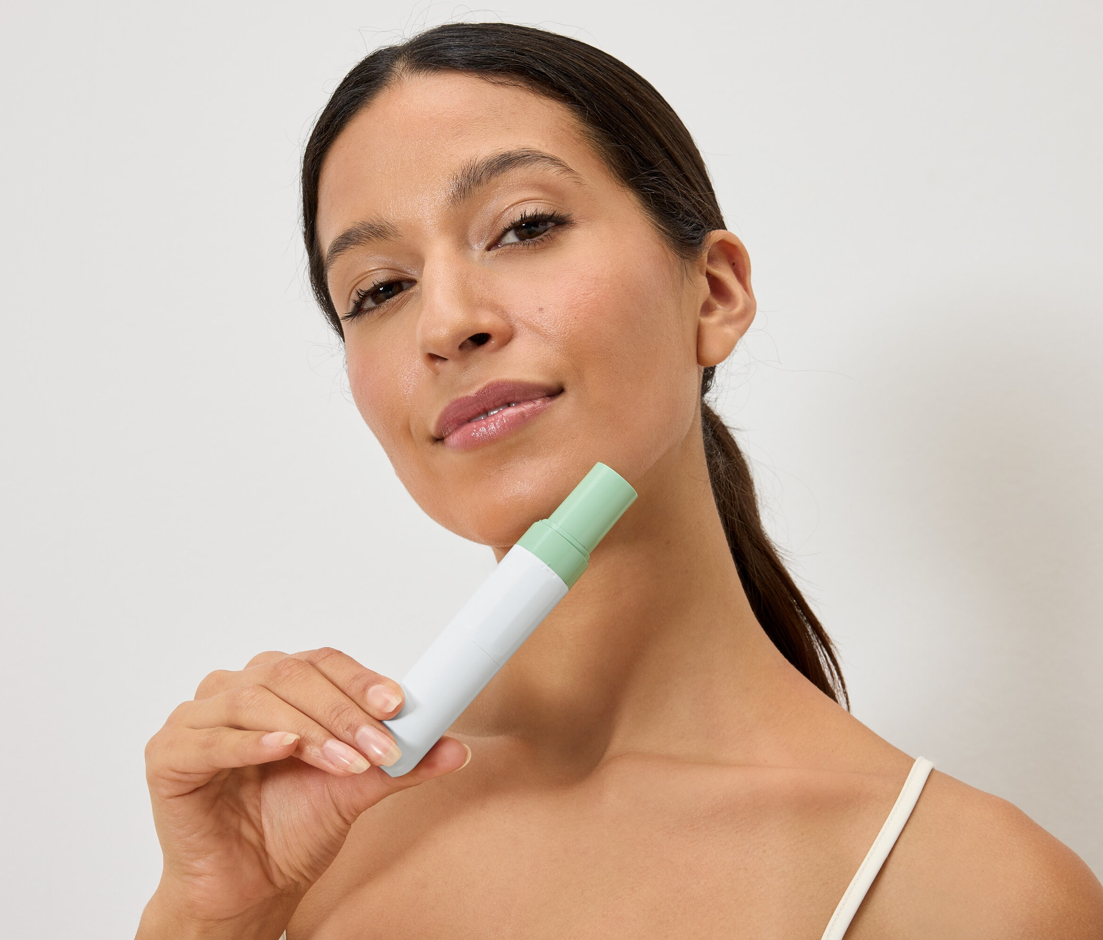 Kadın, yüzünün önünde beyaz ve yeşil bir şişe tutuyor.