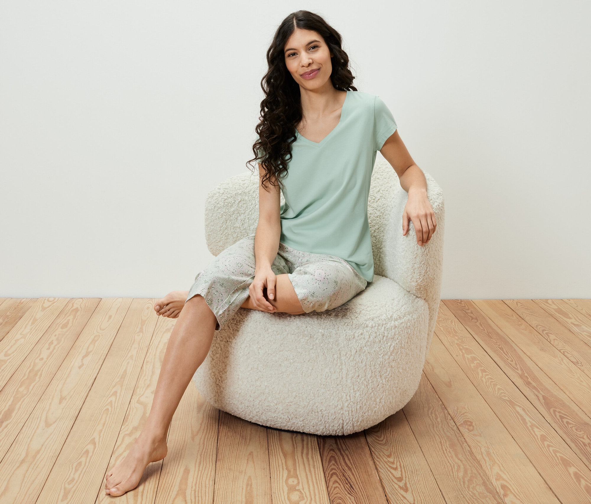 Bir kadın koltukta oturuyor ve açık yeşil renkli 3/4 pijama takımı giyiyor.