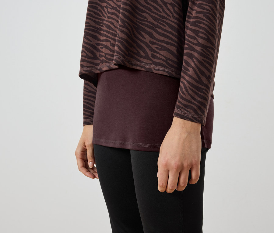 Kahverengi-siyah zebra desenli tunik, bordo bluz ve siyah tayt giyen bir kadının detayı.