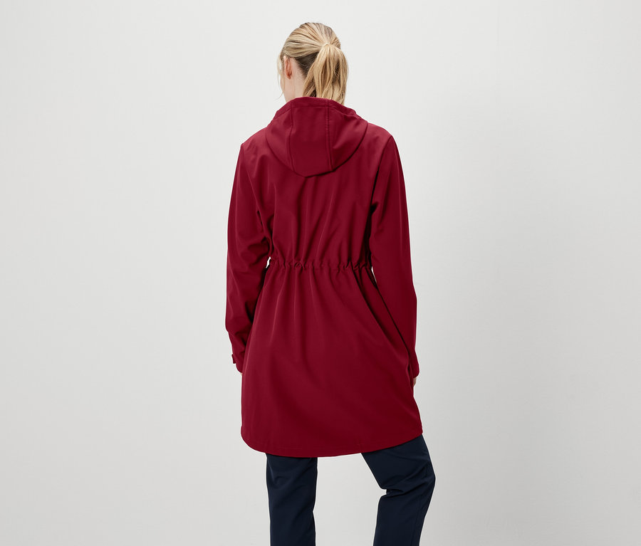 Sırtı kameraya dönük bir kadın, kapüşonlu kırmızı bir ceket ve lacivert pantolon giyiyor.