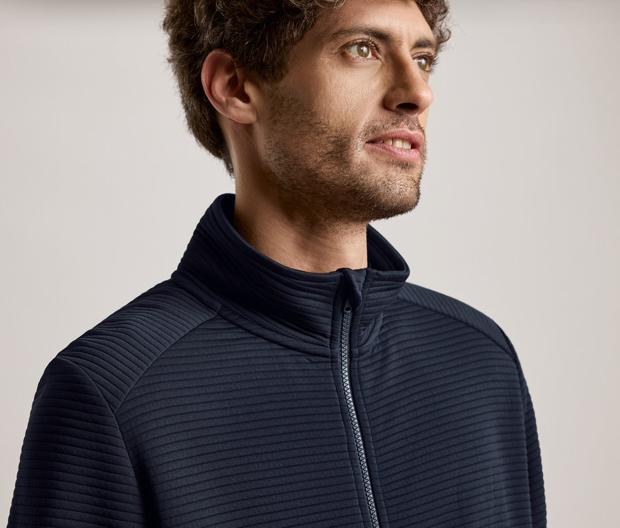 Kıvırcık saçlı, lacivert fermuarlı ceket giyen ve sağa bakan bir adamın yakın çekim portresi.