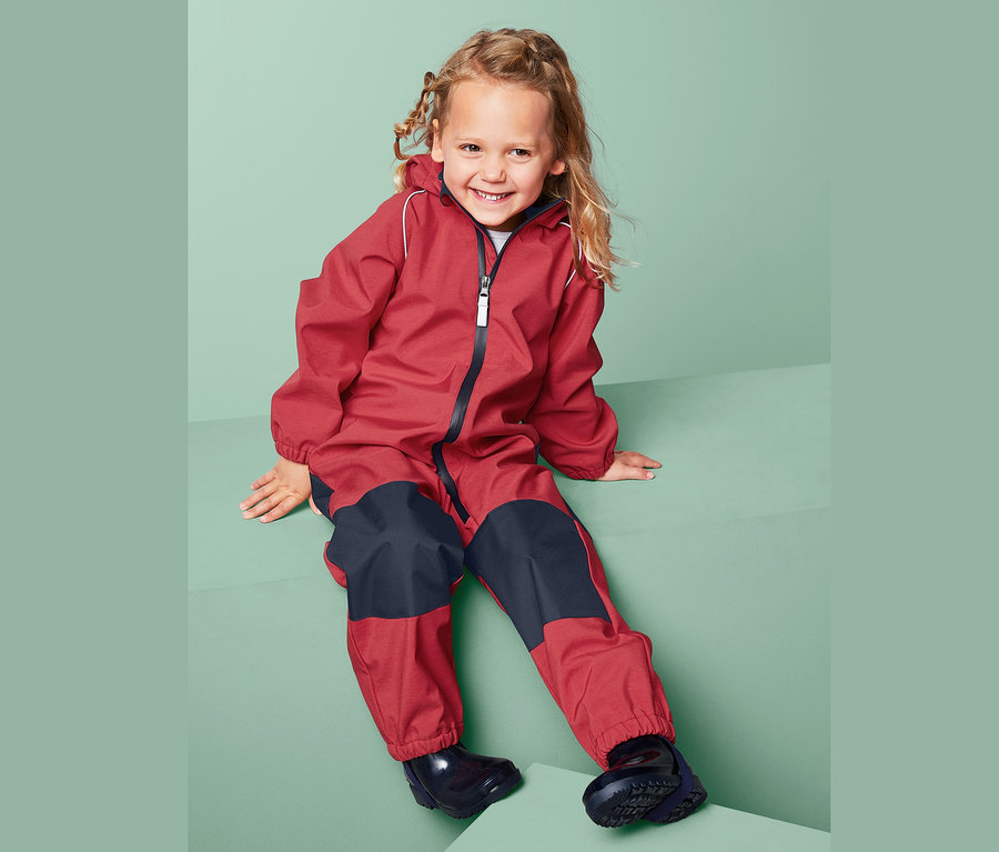 Kız çocuğu kırmızı-lacivert softshell tulum içinde oturuyor.