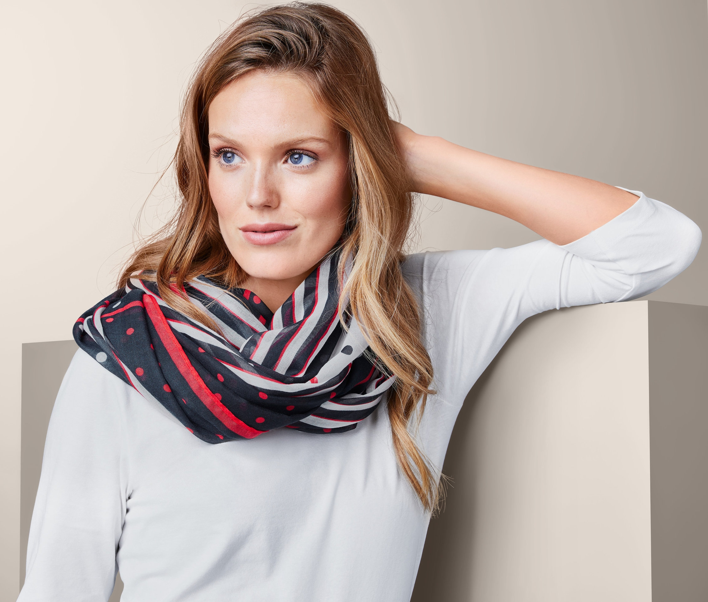 Sarışın saçlı ve mavi gözlü bir kadın, kırmızı, beyaz ve siyah desenli bir boyunluk takıyor.