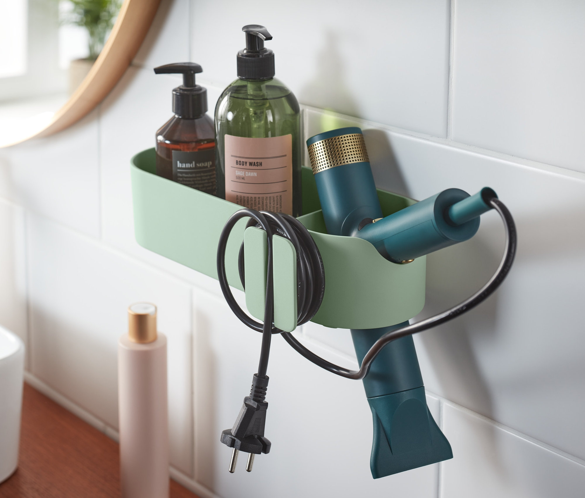 Banyoda beyaz fayansların üzerinde kahverengi sabun, yeşil şişe ve saç kurutma makinesi bulunan yeşil bir banyo düzenleyici asılı duruyor.
