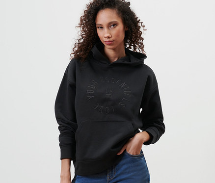 Kadın siyah kapüşonlu sweatshirt ve mavi kot pantolonla poz veriyor.