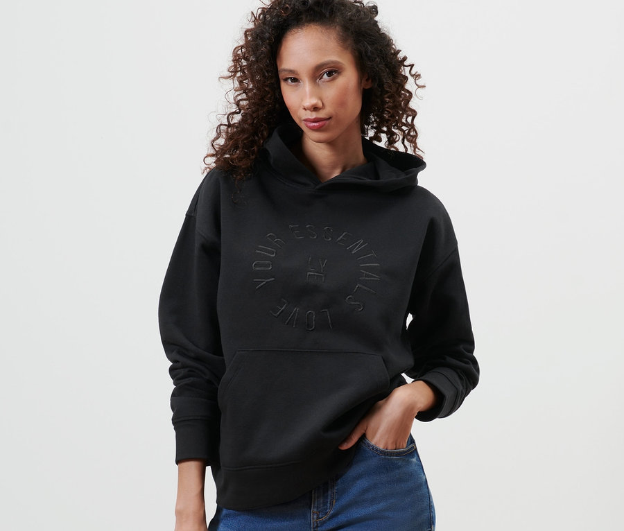 Kadın siyah kapüşonlu sweatshirt ve mavi kot pantolonla poz veriyor.