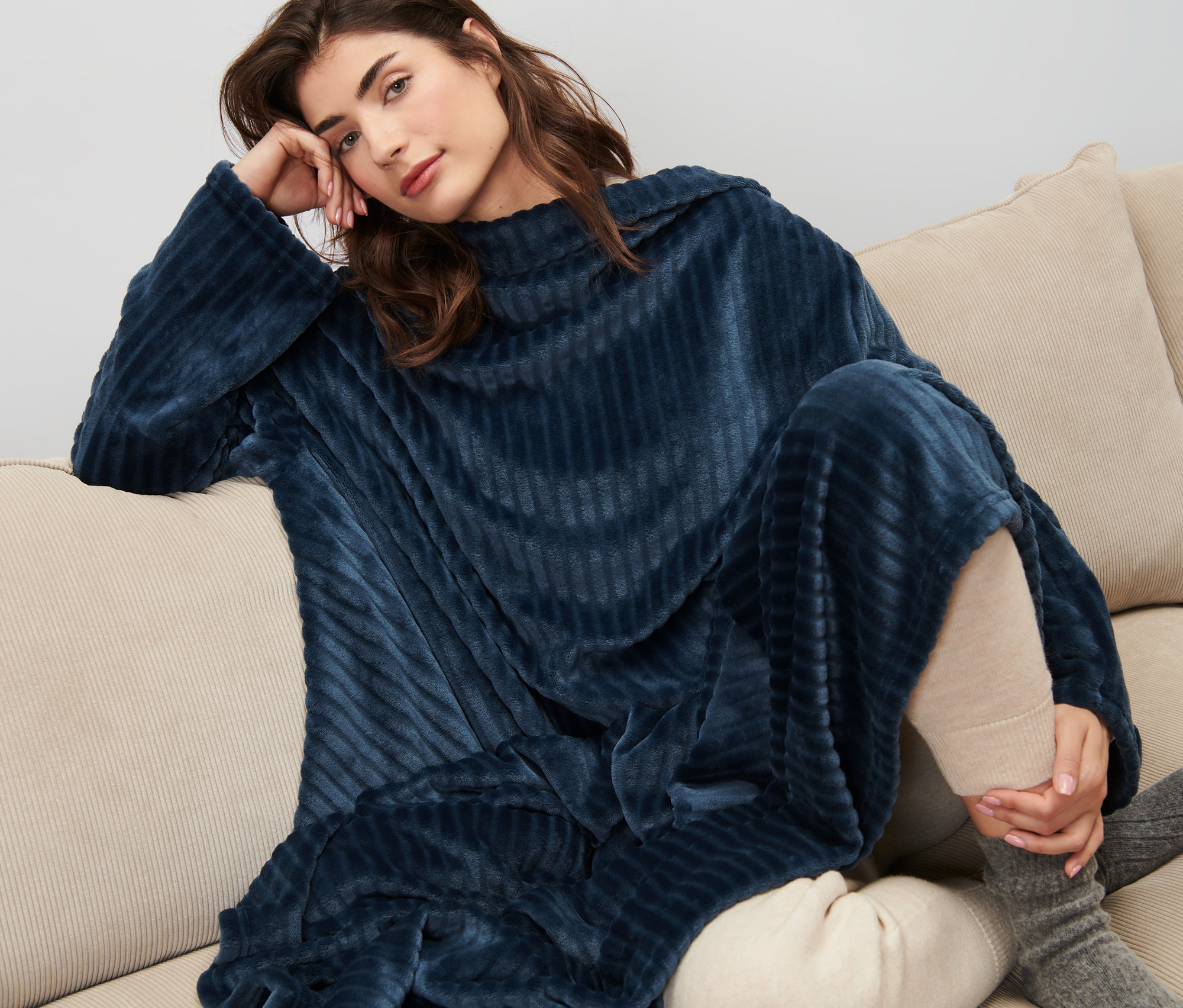 Kadın kanepede oturuyor, üzerinde Entegre Kollu Yumuşak Battaniye var.