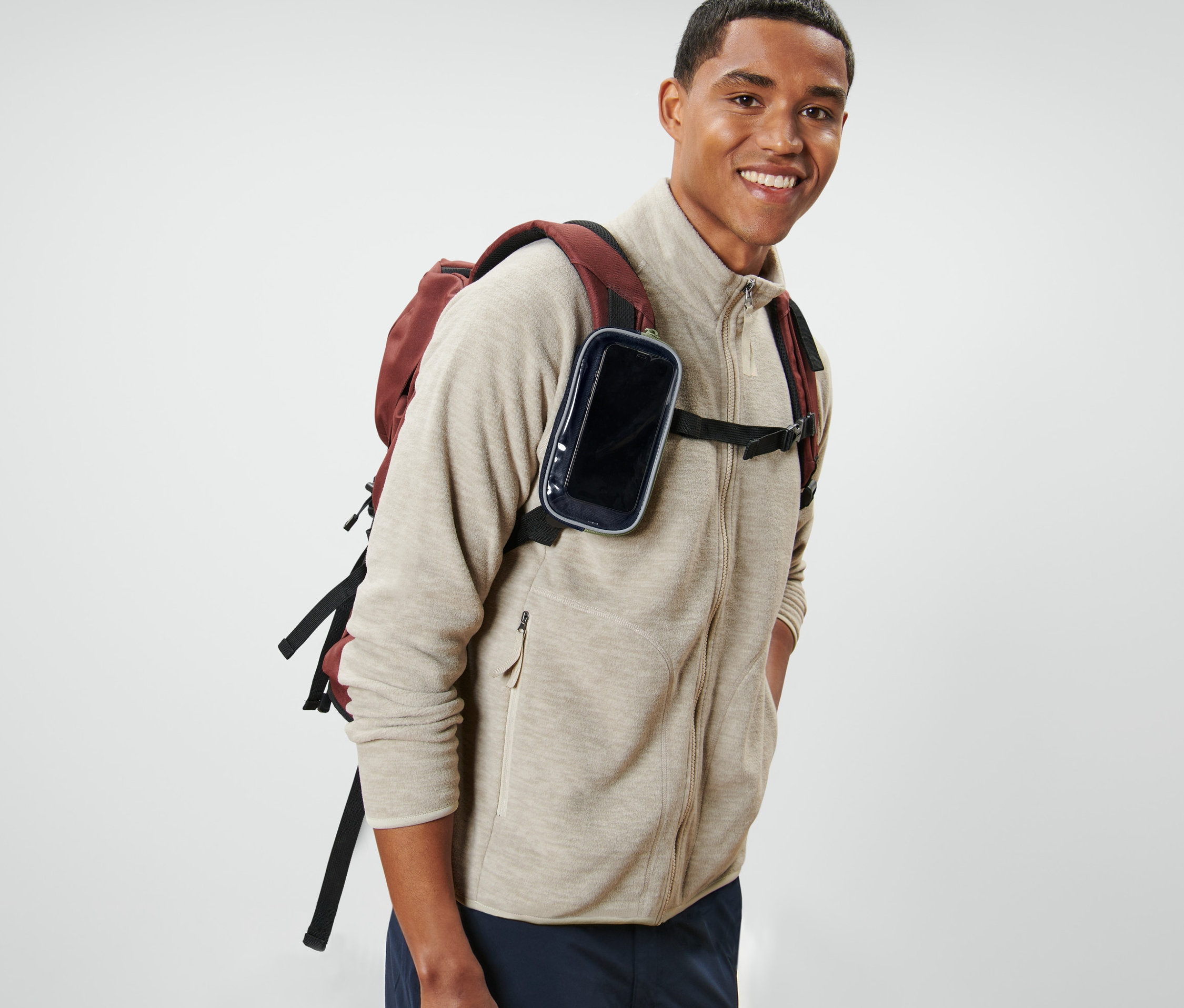 Sırıtarak poz veren bir adam sırt çantası ve saydam yüzeyli çok işlevli çantasıyla birlikte duruyor.