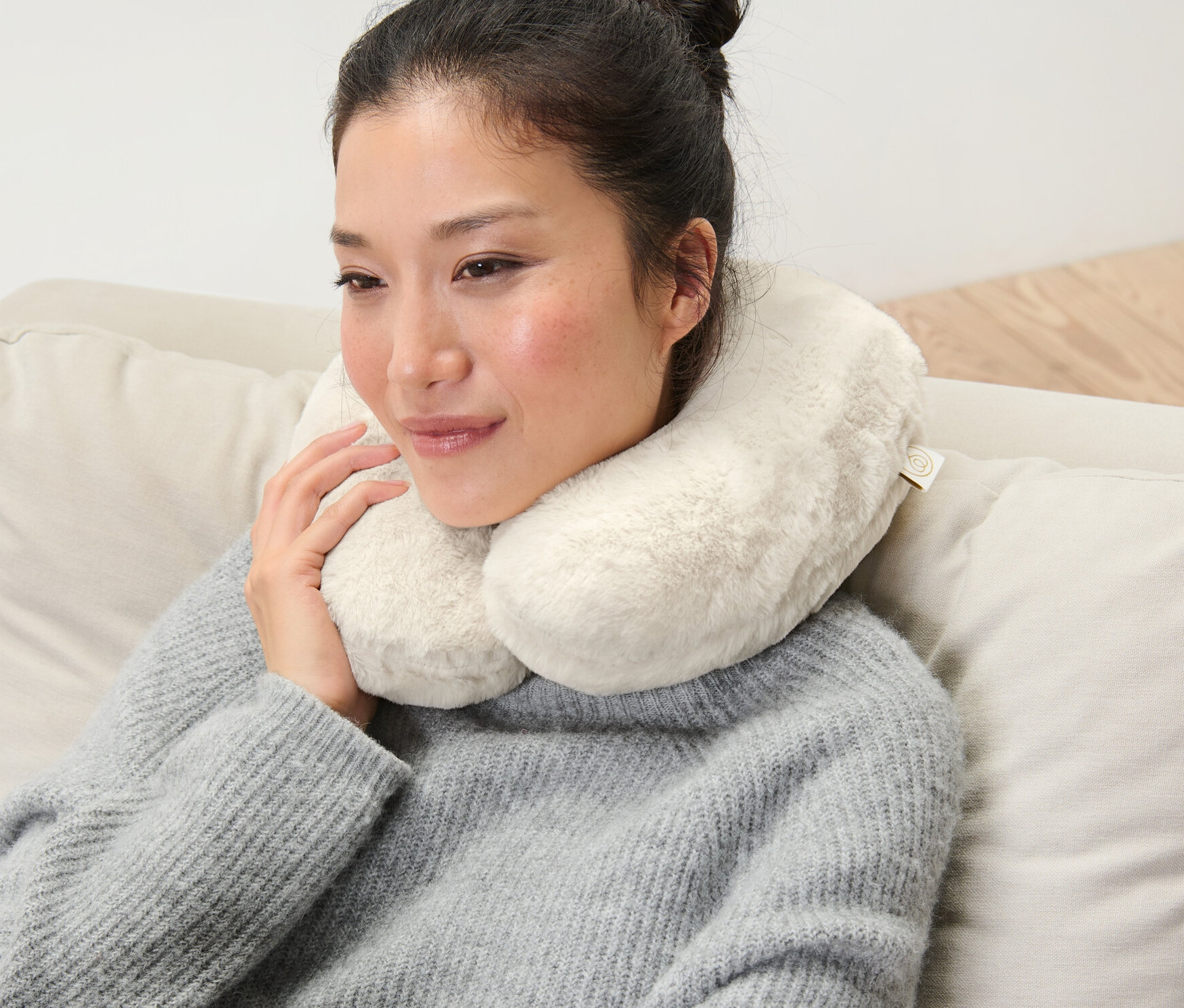 Kadın krem rengi hafızalı süngerli boyun yastığı ile kanepede oturuyor.