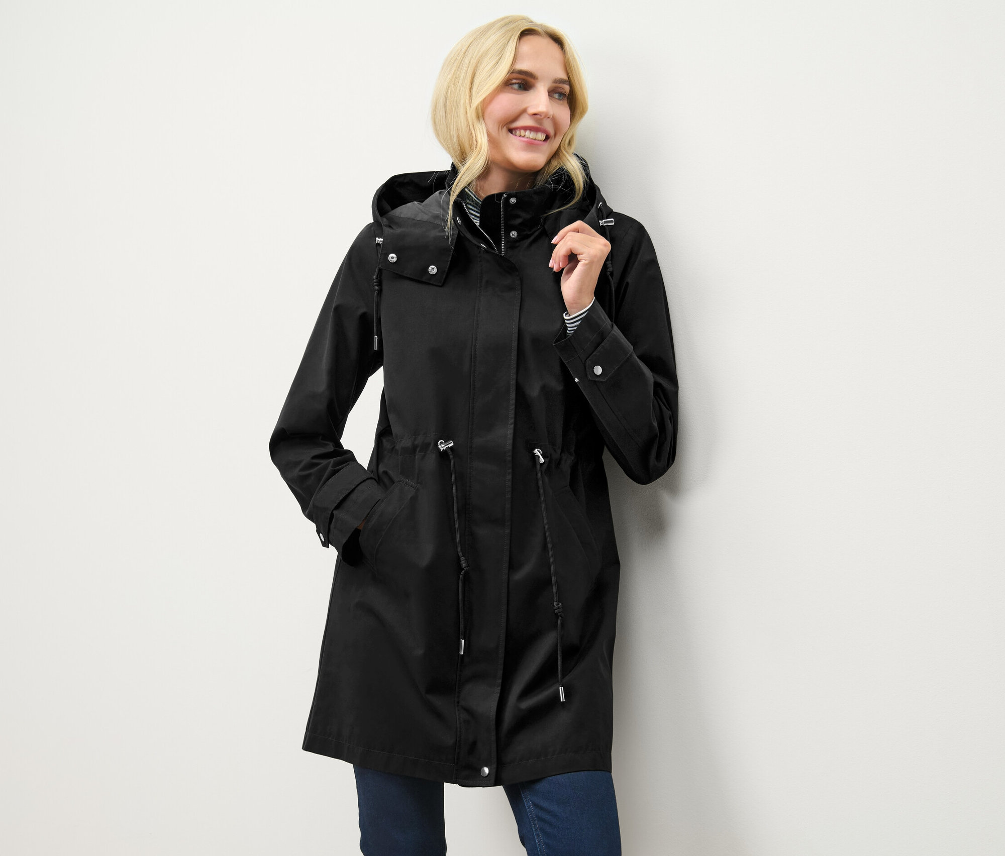 Sarışın bir kadın, siyah kapüşonlu bir parkayla poz veriyor.