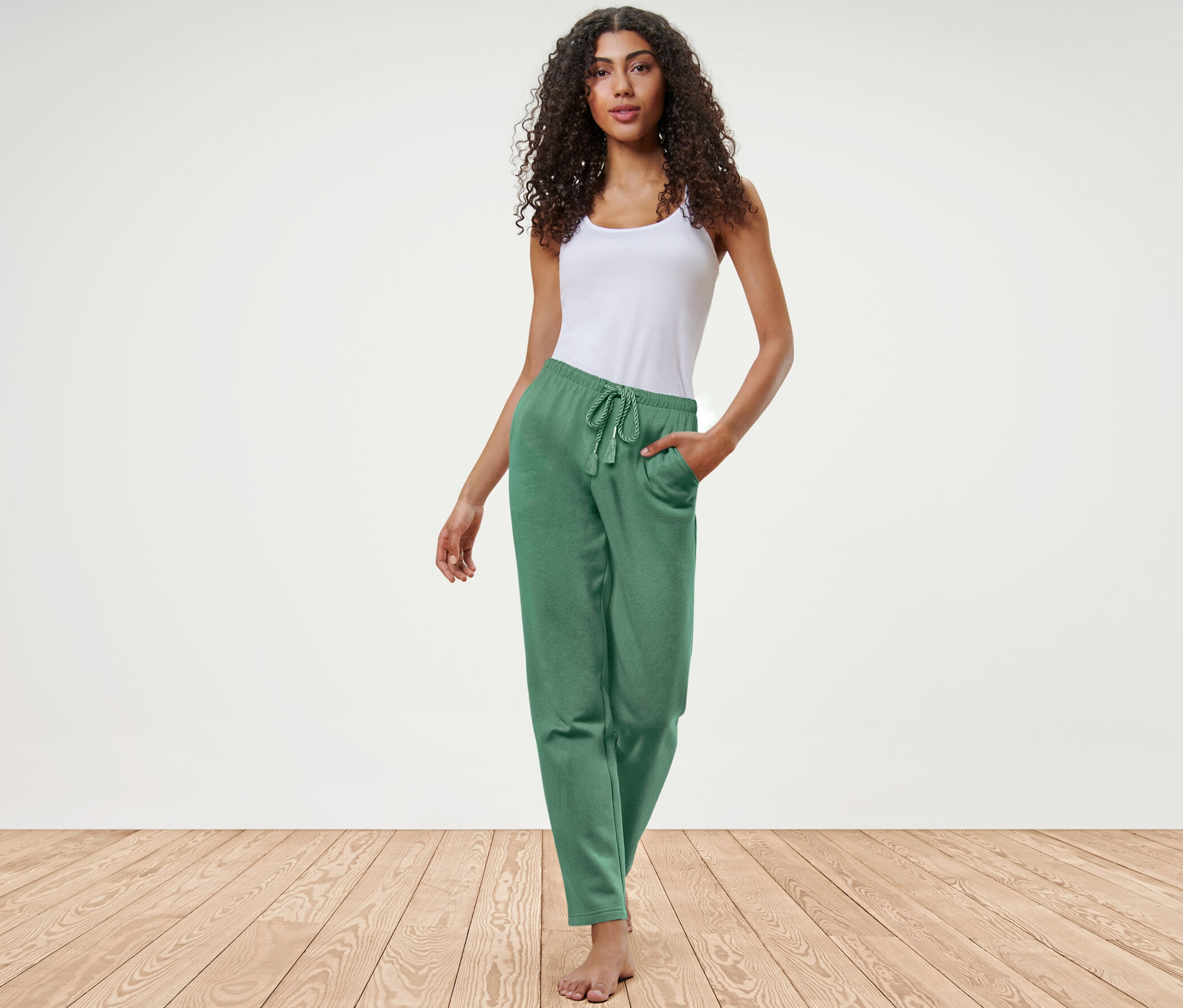 Kadın, yeşil eşofman altı ve beyaz atletle poz veriyor.